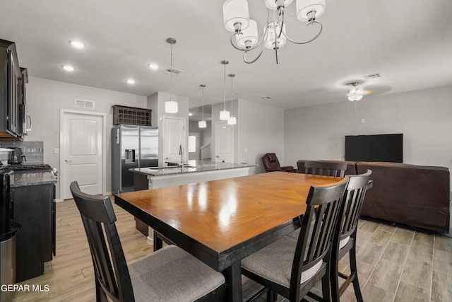 dining space featuring ceiling fan with notable chandelier, light hardwood / wood-style floors, and sink