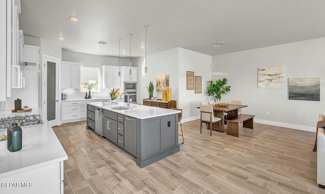 kitchen featuring white cabinets, tasteful backsplash, an island with sink, gray cabinets, and appliances with stainless steel finishes