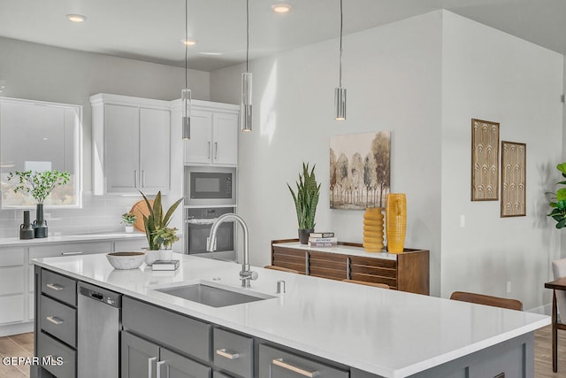 kitchen with a center island with sink, stainless steel appliances, decorative light fixtures, backsplash, and sink