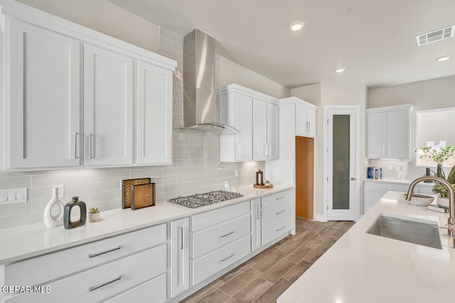 kitchen with wall chimney range hood, light hardwood / wood-style floors, white cabinets, stainless steel gas cooktop, and tasteful backsplash