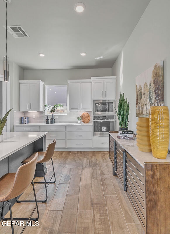 kitchen featuring light hardwood / wood-style flooring, stainless steel appliances, backsplash, hanging light fixtures, and white cabinetry