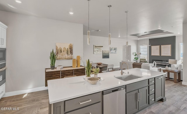 kitchen with gray cabinetry, sink, stainless steel dishwasher, and a kitchen island with sink