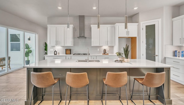 kitchen with a wealth of natural light, tasteful backsplash, a center island with sink, and wall chimney exhaust hood