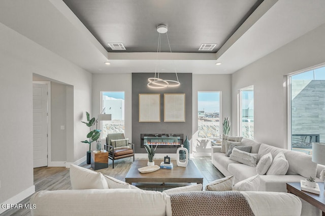 living room with a healthy amount of sunlight, light hardwood / wood-style floors, and a raised ceiling