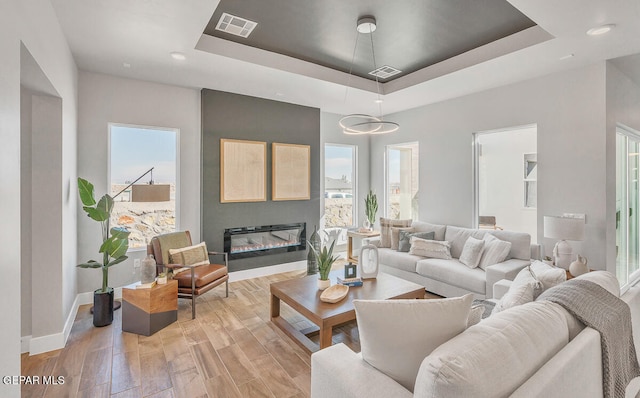 living room with light hardwood / wood-style floors and a raised ceiling