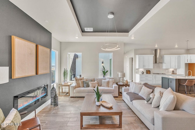 living room with sink, light hardwood / wood-style flooring, and a raised ceiling