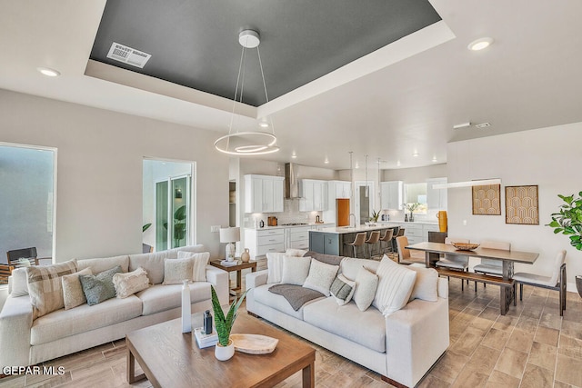 living room with light wood-type flooring and a raised ceiling