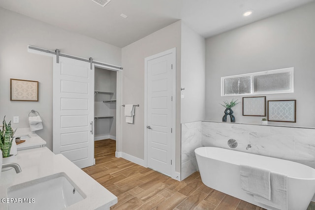 bathroom with tile walls, wood-type flooring, vanity, and a bath to relax in