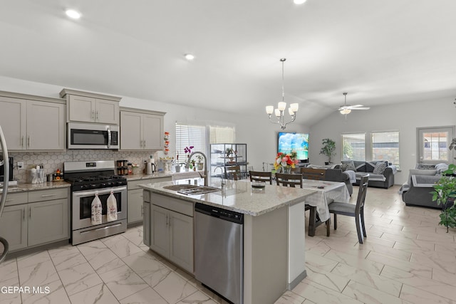 kitchen with tasteful backsplash, lofted ceiling, gray cabinets, a kitchen island with sink, and appliances with stainless steel finishes