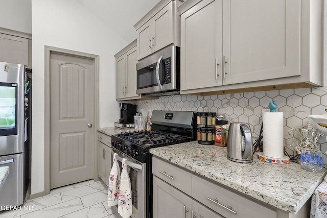 kitchen featuring decorative backsplash, light stone counters, gray cabinetry, stainless steel appliances, and lofted ceiling