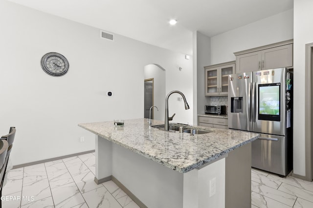 kitchen featuring light stone countertops, stainless steel fridge with ice dispenser, sink, and an island with sink