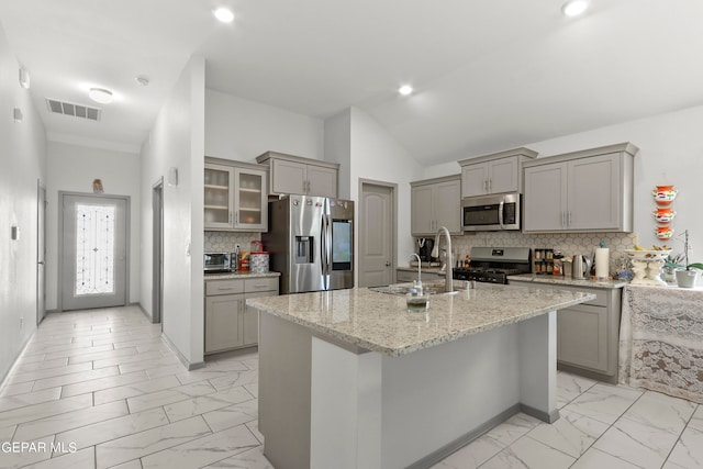 kitchen featuring light stone countertops, stainless steel appliances, a kitchen island with sink, and sink