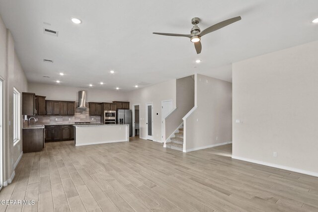 kitchen with light hardwood / wood-style flooring, a center island, wall chimney range hood, appliances with stainless steel finishes, and ceiling fan