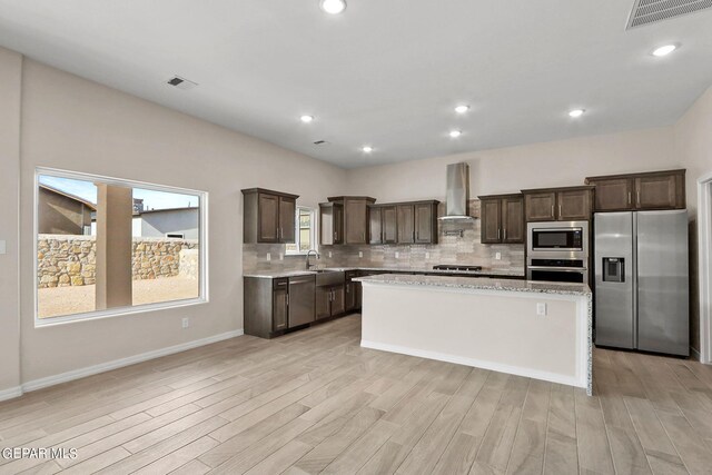 kitchen featuring appliances with stainless steel finishes, wall chimney range hood, light hardwood / wood-style flooring, and a center island