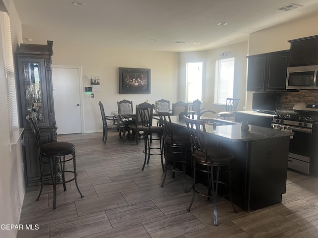 kitchen featuring dark stone counters, range with gas stovetop, backsplash, a center island, and a kitchen bar