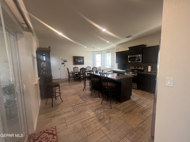 kitchen featuring tasteful backsplash, a breakfast bar area, a center island with sink, lofted ceiling, and appliances with stainless steel finishes