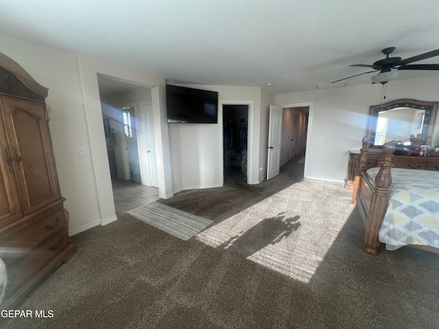 bedroom with ceiling fan, a walk in closet, a closet, and dark colored carpet