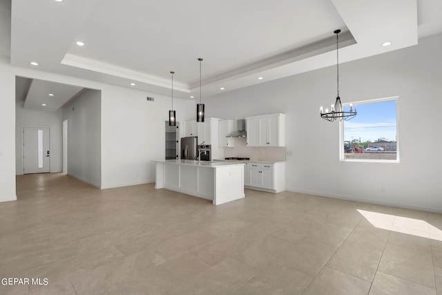 kitchen featuring wall chimney exhaust hood, white cabinetry, a raised ceiling, and hanging light fixtures