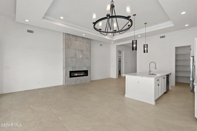 kitchen with decorative light fixtures, an island with sink, a raised ceiling, and white cabinetry