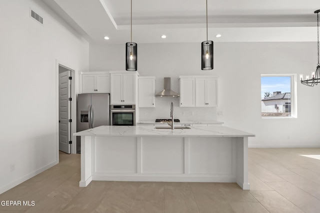 kitchen with white cabinets, hanging light fixtures, wall chimney exhaust hood, appliances with stainless steel finishes, and light stone countertops