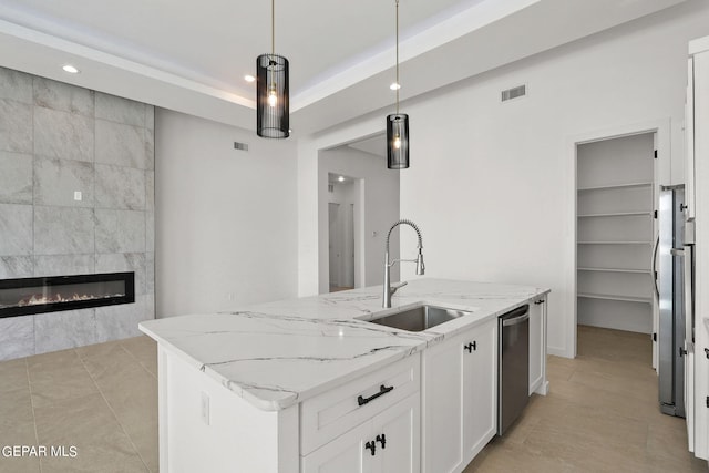 kitchen featuring appliances with stainless steel finishes, white cabinets, light stone countertops, pendant lighting, and a center island with sink