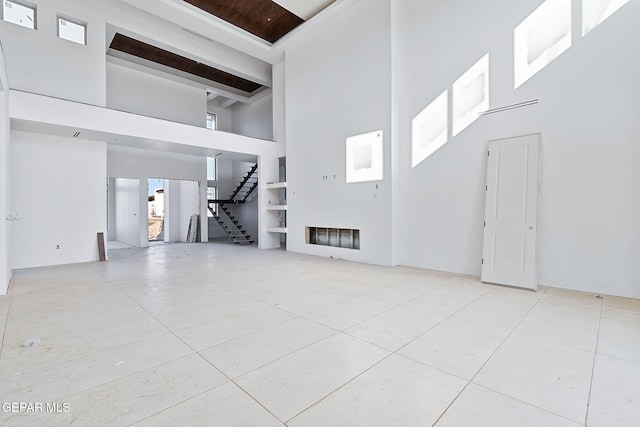 unfurnished living room featuring visible vents, stairway, tile patterned flooring, and a towering ceiling