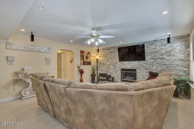 living room with a stone fireplace and ceiling fan