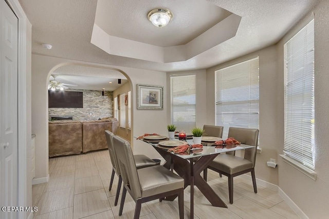 tiled dining space with a textured ceiling, a tray ceiling, and ceiling fan