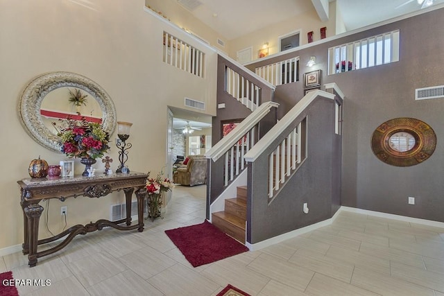 stairs with beam ceiling, ceiling fan, tile patterned floors, and a high ceiling