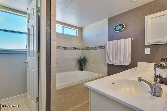 bathroom featuring tiled tub, vanity, and a textured ceiling