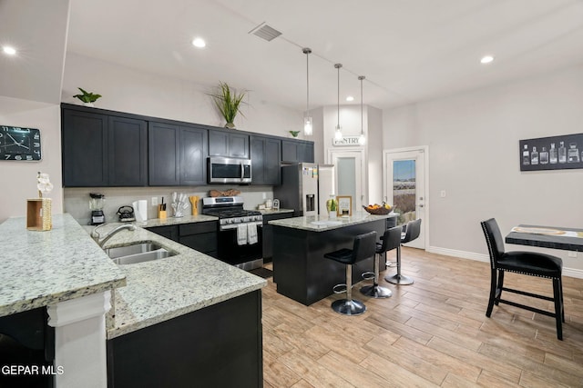 kitchen featuring light stone countertops, sink, hanging light fixtures, a kitchen island, and appliances with stainless steel finishes