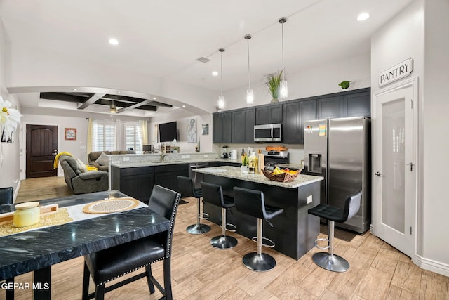 kitchen featuring pendant lighting, appliances with stainless steel finishes, beamed ceiling, a kitchen island, and a breakfast bar area