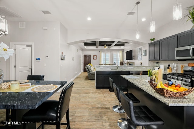 kitchen with light stone countertops, hanging light fixtures, beamed ceiling, a kitchen bar, and appliances with stainless steel finishes