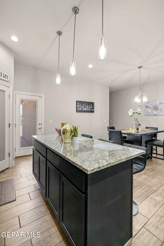 kitchen featuring a notable chandelier, a center island, light stone counters, and hanging light fixtures