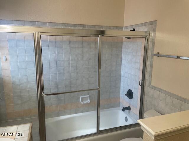 bathroom featuring enclosed tub / shower combo, tile walls, and toilet