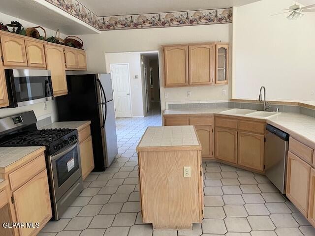 kitchen with appliances with stainless steel finishes, sink, light brown cabinets, tile countertops, and a kitchen island