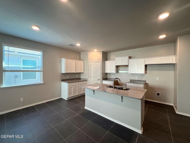 kitchen featuring dark tile patterned flooring, an island with sink, white cabinetry, and sink