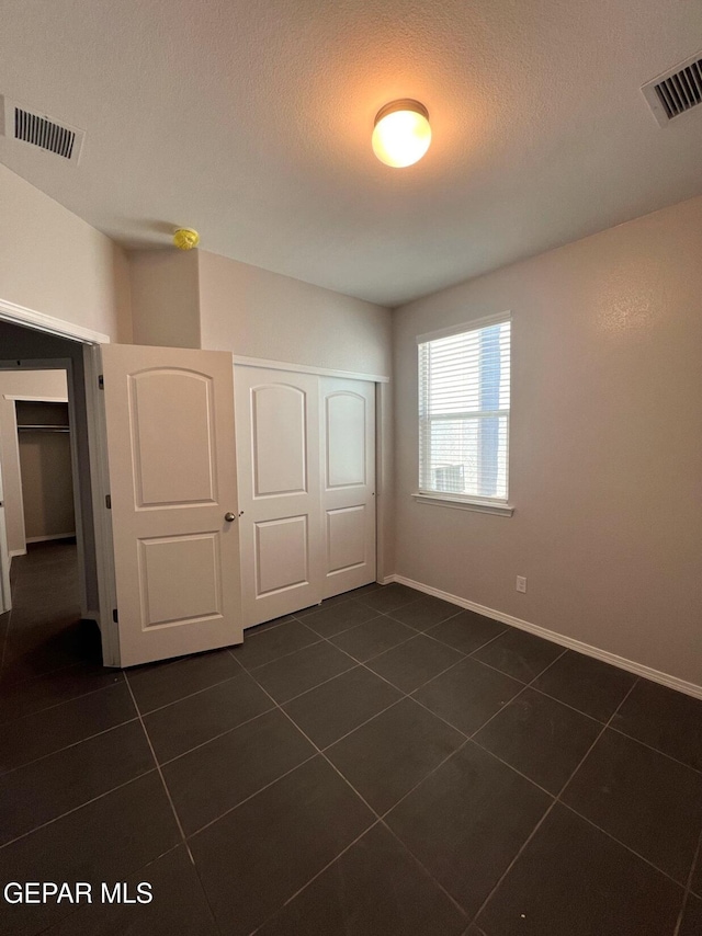 unfurnished bedroom featuring a closet, dark tile patterned floors, and a textured ceiling