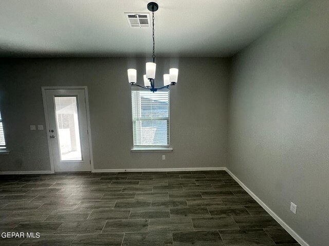 unfurnished dining area with dark wood-type flooring, a chandelier, and a wealth of natural light