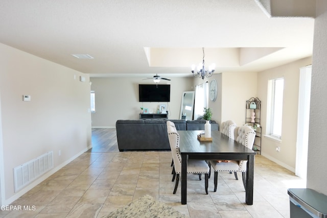 dining room with ceiling fan with notable chandelier and a tray ceiling