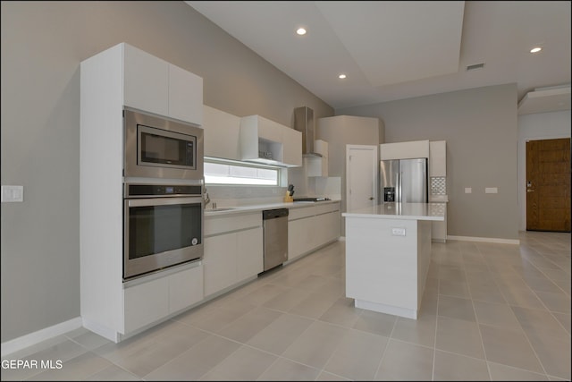 kitchen with appliances with stainless steel finishes, wall chimney exhaust hood, light tile patterned floors, a center island, and white cabinetry