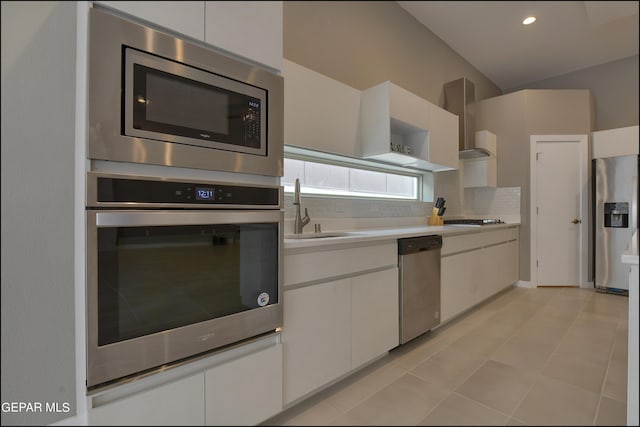 kitchen featuring appliances with stainless steel finishes, wall chimney exhaust hood, sink, white cabinetry, and lofted ceiling