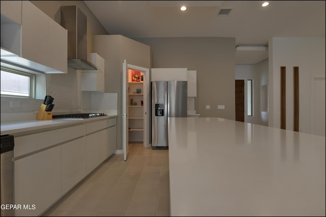 kitchen with tasteful backsplash, white cabinets, wall chimney range hood, and appliances with stainless steel finishes