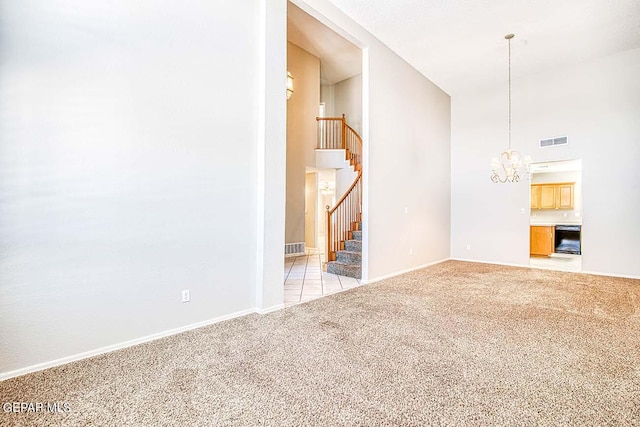 unfurnished living room with a towering ceiling, an inviting chandelier, and light carpet