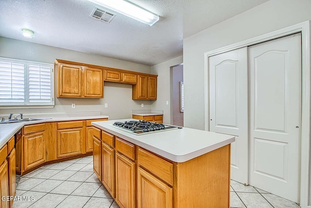 kitchen featuring stainless steel gas cooktop, light tile floors, a center island, sink, and a textured ceiling