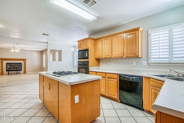 kitchen with light tile flooring, a tiled fireplace, black appliances, sink, and pendant lighting