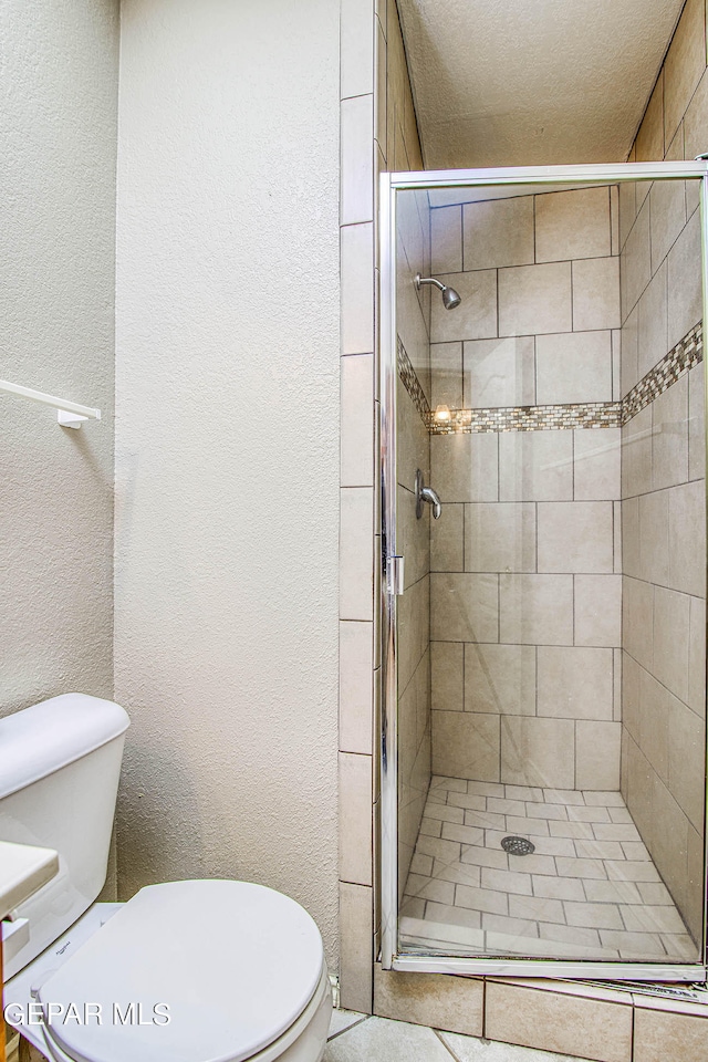 bathroom featuring a shower with door, toilet, and a textured ceiling