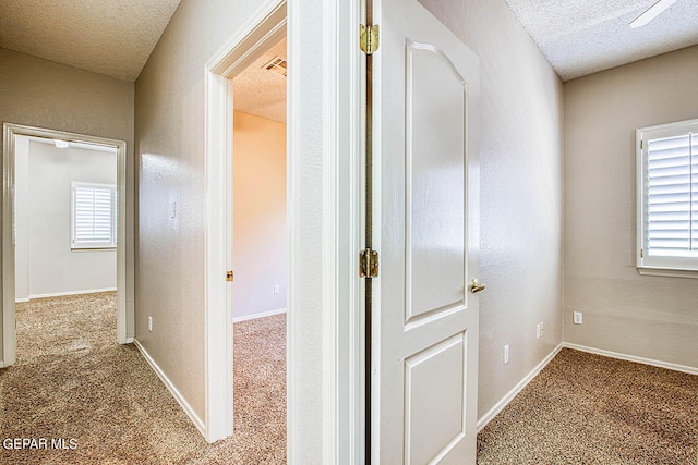 hallway with a textured ceiling and carpet flooring