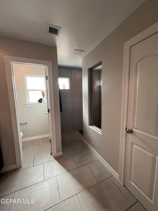 hallway with light tile patterned floors, baseboards, visible vents, and a textured ceiling