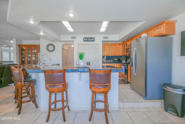 kitchen with a center island with sink, a kitchen breakfast bar, a raised ceiling, sink, and stainless steel appliances